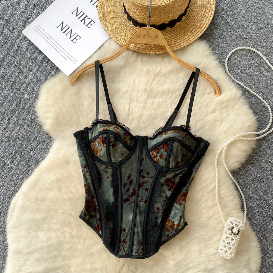 Black lace corset on a hanger with a straw hat and pearl necklace on a textured surface