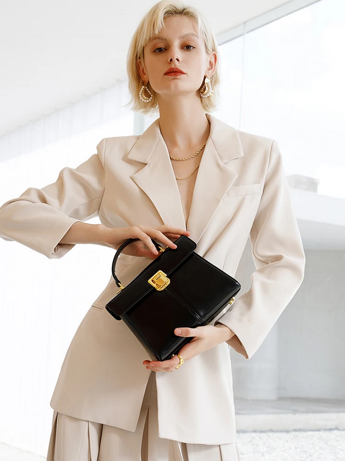 Woman in a beige suit holding a black handbag indoors